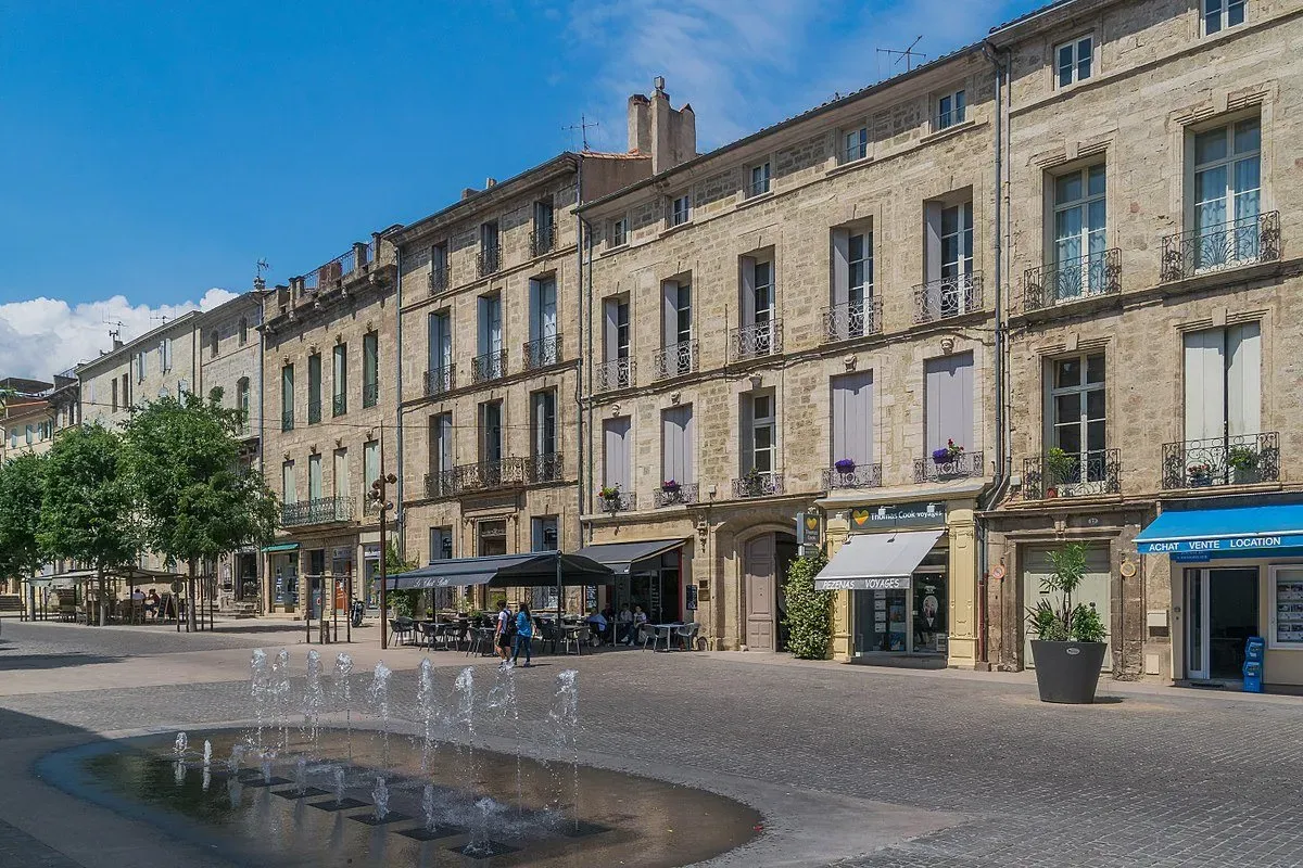 Place de ville historique à Pézenas avec façades anciennes et jet d'eau.
